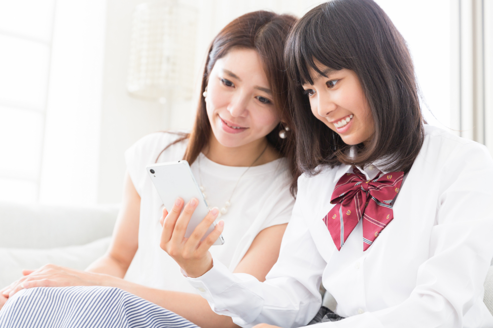 女子高生と母親が笑顔でスマートフォンを眺める写真